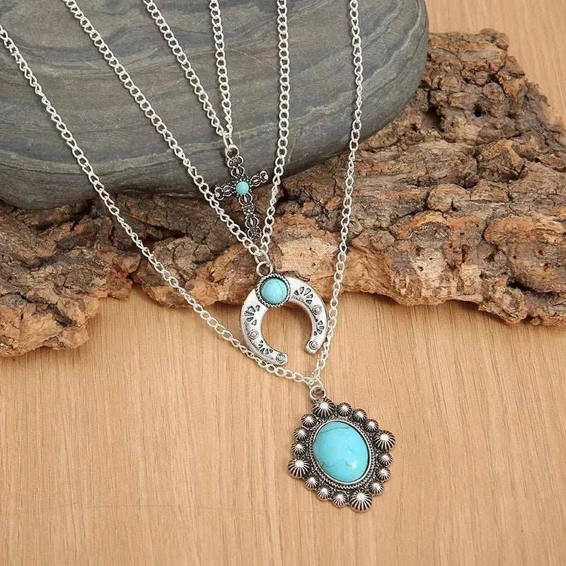 Three-layered alloy turquoise necklace with intricate pendants and artificial turquoise stones on silver chains displayed on rustic wood background