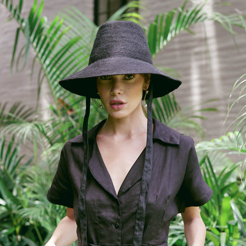 Black MEG jute straw hat with tall crown and medium brim worn by woman in dark outfit outdoors